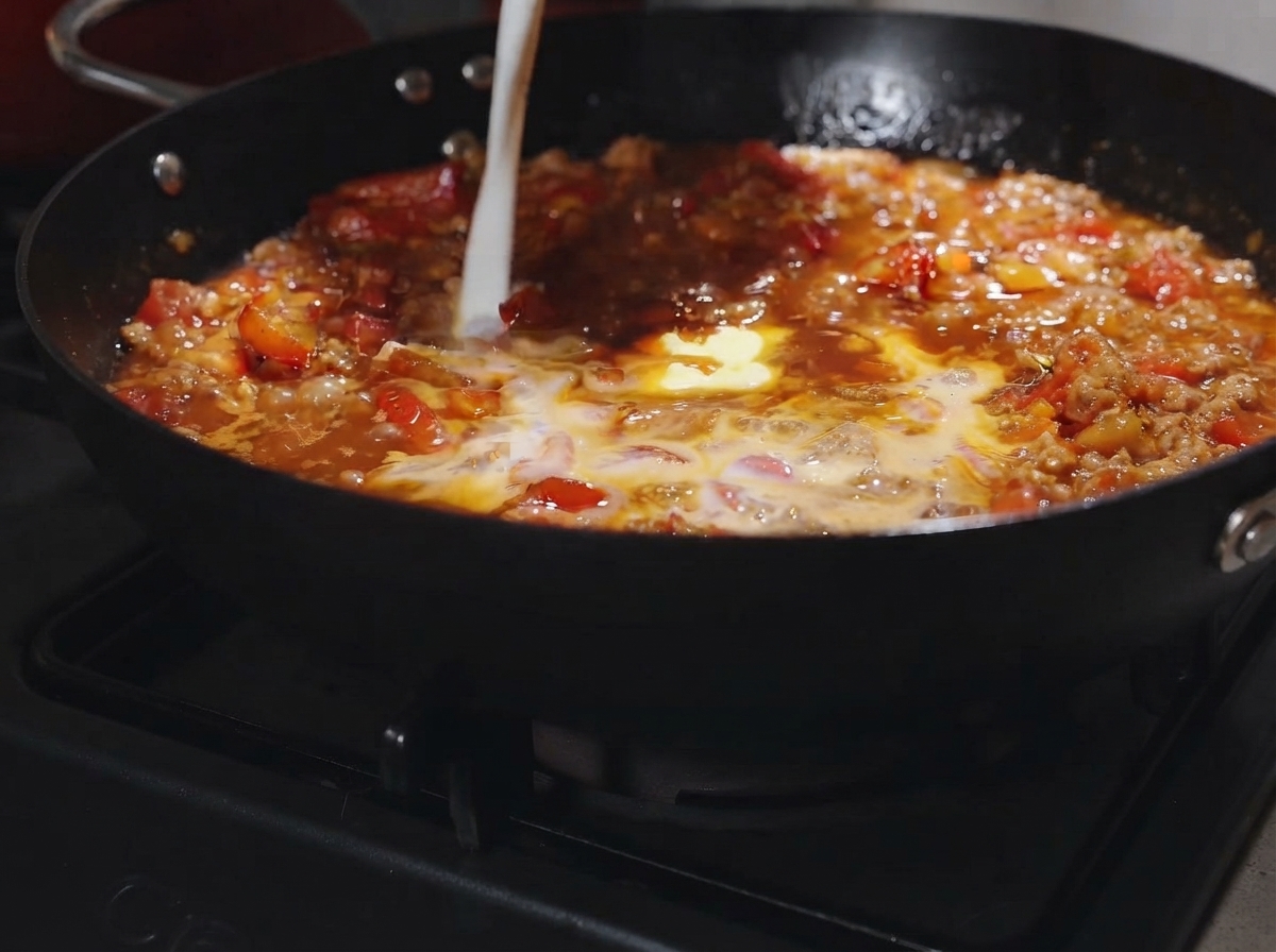 끓고 있는 토마토 미트 소스에 버터 한 조각과 우유를 붓는 모습.