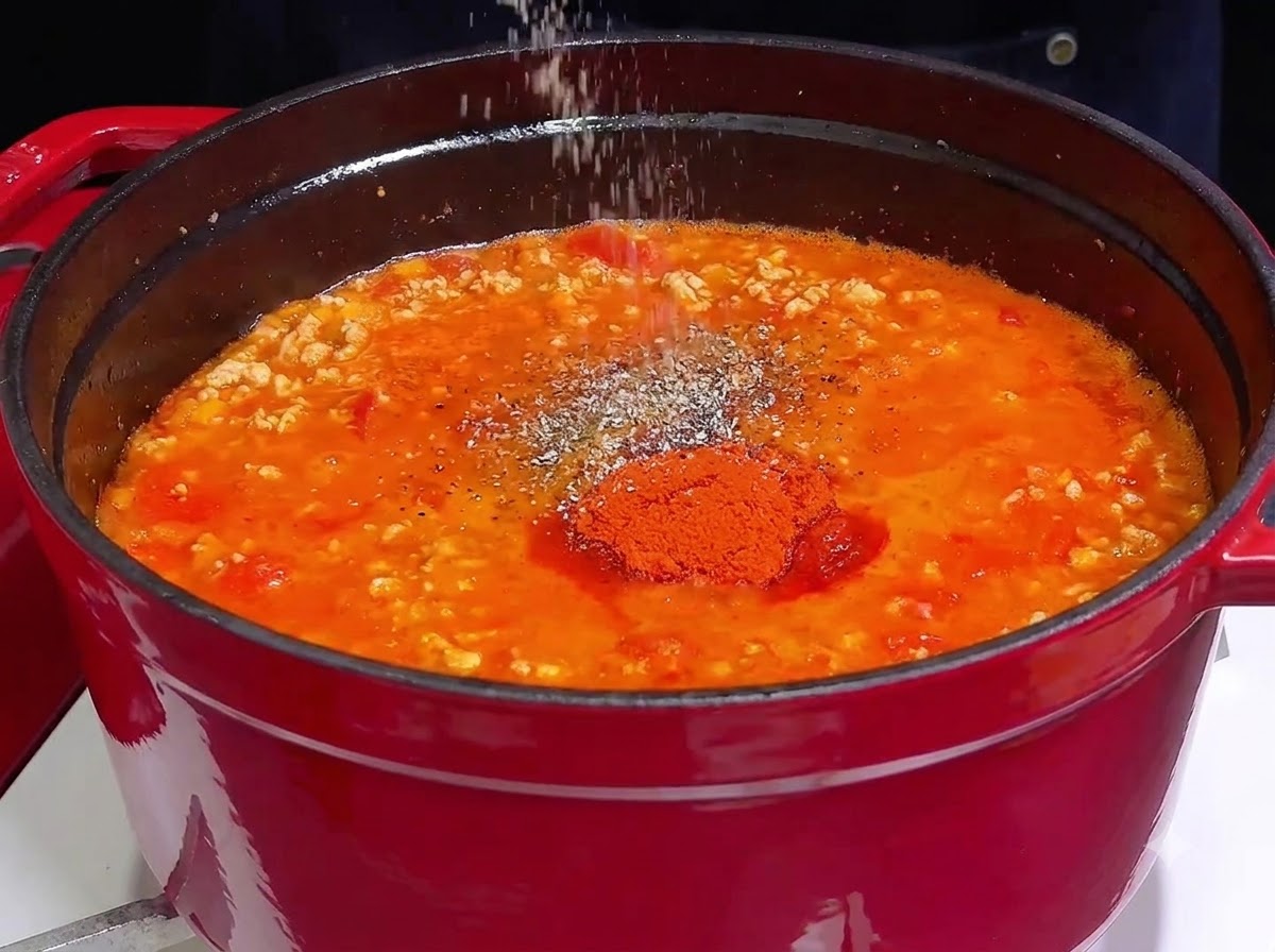 무쇠 냄비에서 보글보글 끓고 있는 강렬한 붉은색 고기 소스에 소금과 향신료를 뿌리는 손.