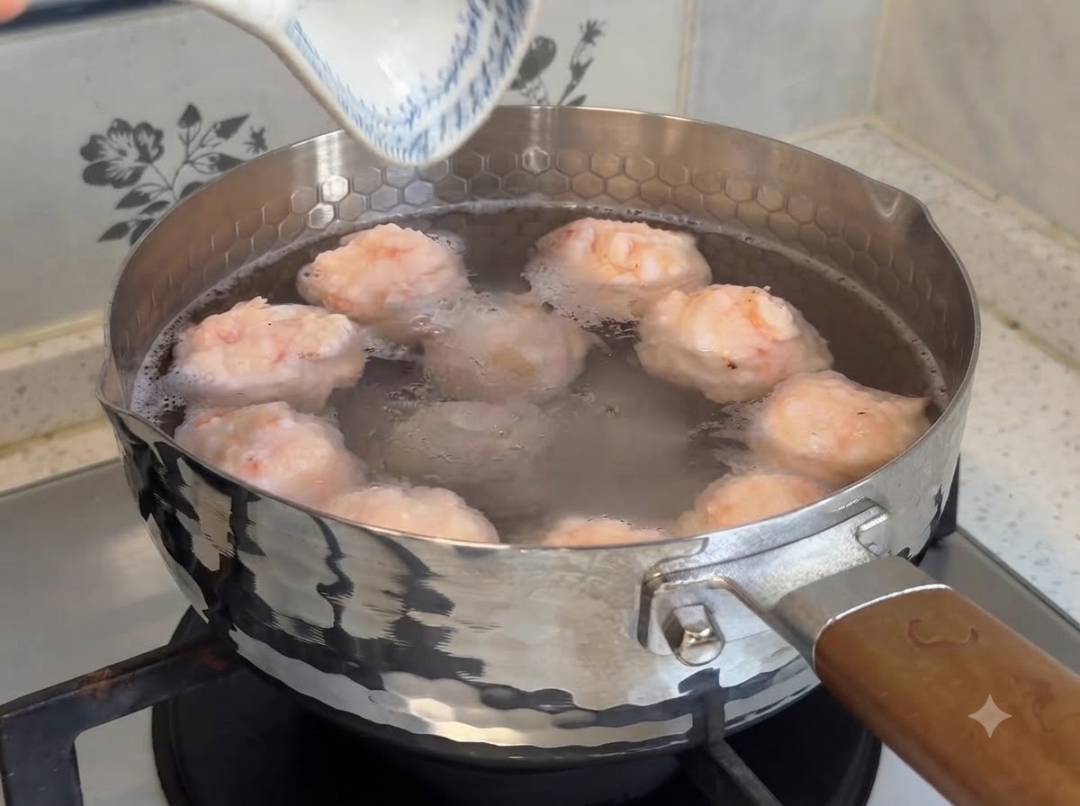 스토브 위 따뜻한 물이 담긴 냄비에서 끓고 있는 통통한 수제 새우완자들의 모습.