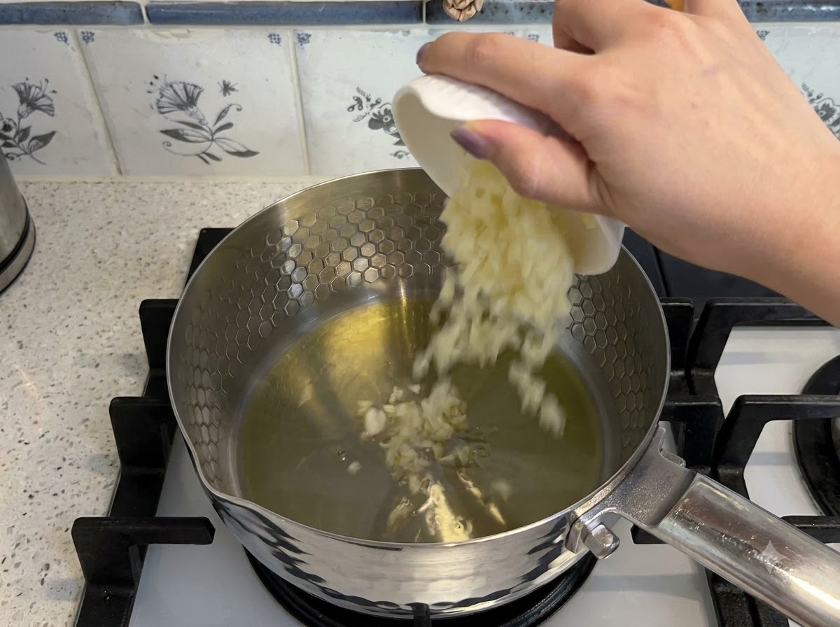 냄비의 뜨거운 기름에 다진 마늘과 썬 토마토를 넣고 볶는 모습.