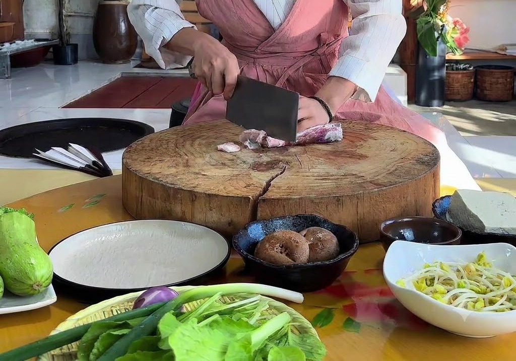 커다란 둥근 나무 도마 위에서 칼로 생삼겹살을 썰고 있는 손.
