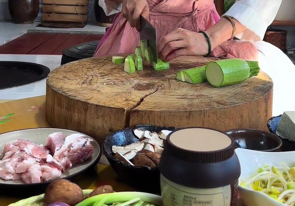 둥근 나무 도마 위에서 칼로 애호박을 삼각형 모양으로 썰고 있는 손.