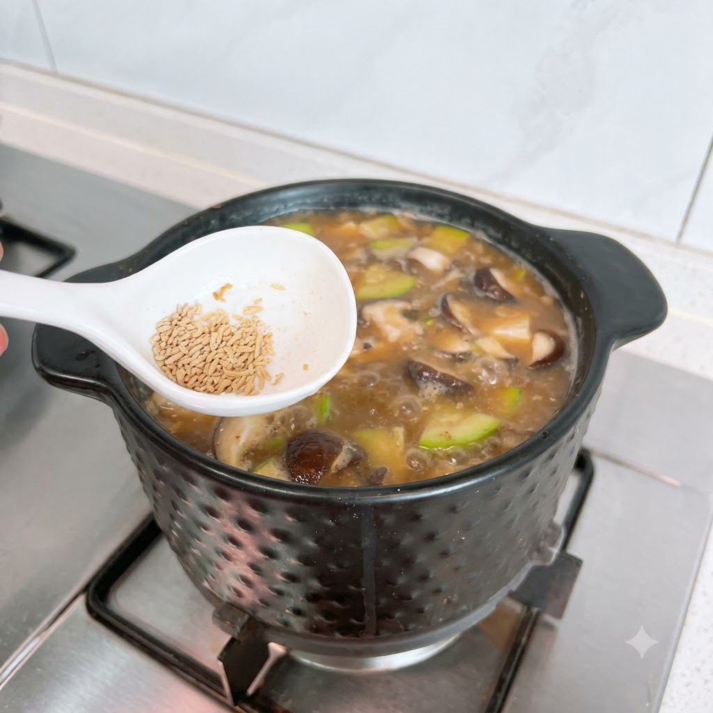 보글보글 끓는 된장찌개 냄비 위에서 하얀 숟가락에 소고기 조미료 분말을 담고 있는 모습.