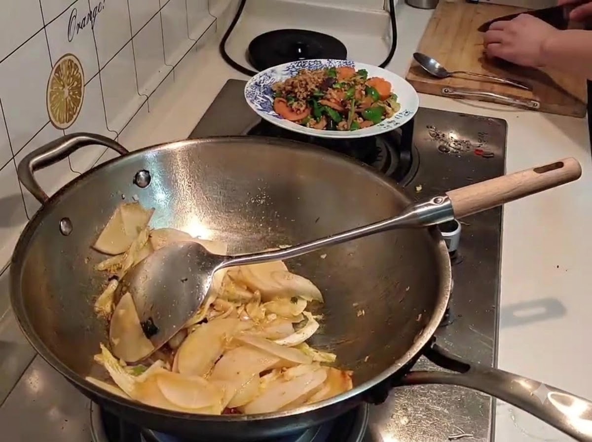 썰어둔 무와 배추가 담긴 웍에 검은색 주전자에서 물을 따르고 있는 모습.
