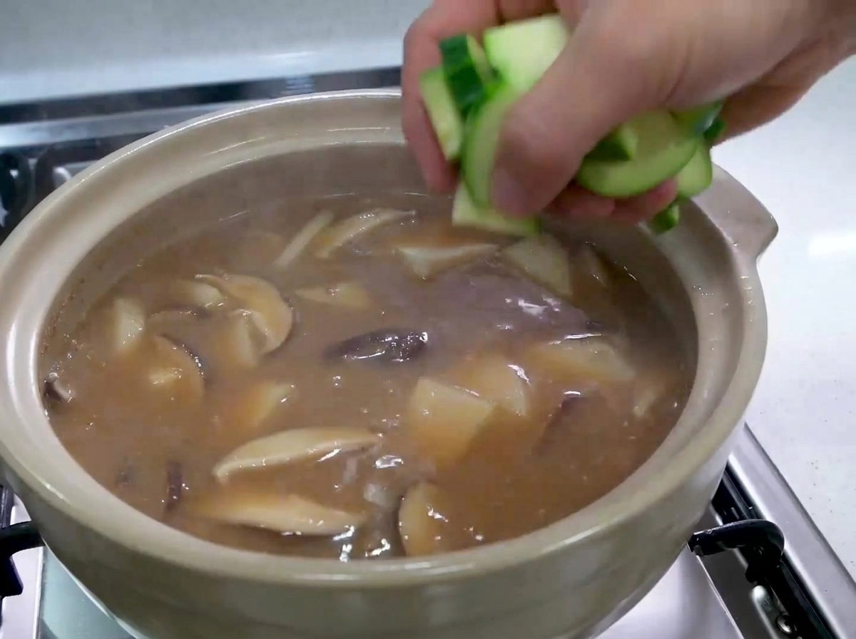 끓고 있는 한국식 찌개에 썬 생 녹색 애호박 조각을 넣는 모습.