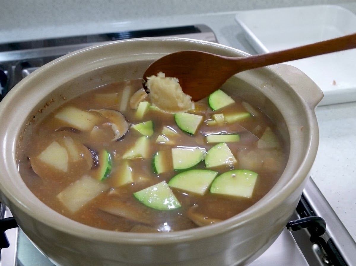 애호박 조각이 가득한 끓는 찌개 위로 다진 마늘을 올린 숟가락을 들고 있는 모습.