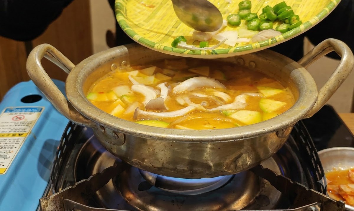 쟁반에 있던 손질된 채소들이 끓고 있는 찌개 냄비 속으로 미끄러져 들어가는 모습.