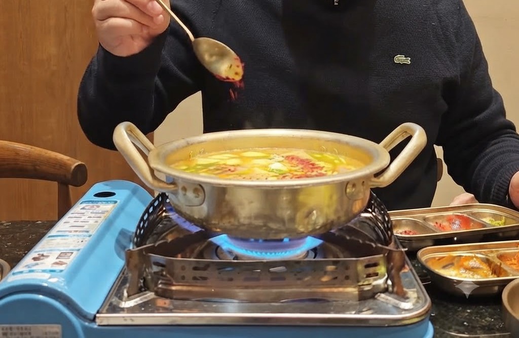 채소와 육수가 보글보글 끓는 냄비 위로 붉은 고춧가루 한 스푼이 뿌려지는 모습.
