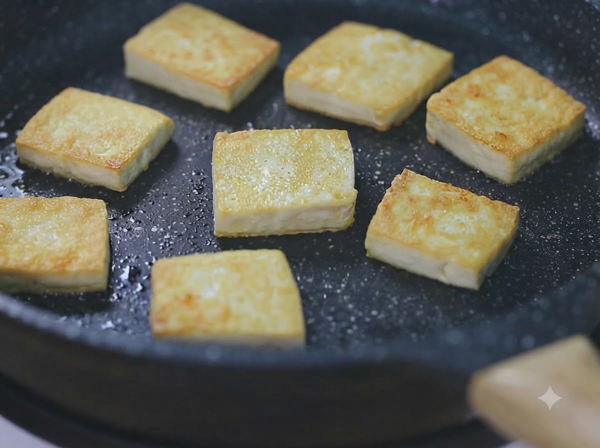 약불에 올린 검은색 프라이팬에서 노릇노릇하게 구워지고 있는 두부 큐브들.