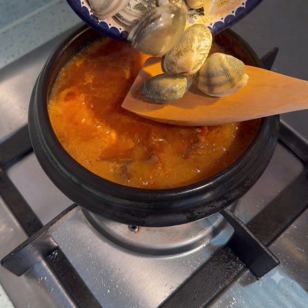 작은 접시에 담긴 생바지락이 끓고 있는 순두부찌개 냄비로 털어 넣어지는 모습.