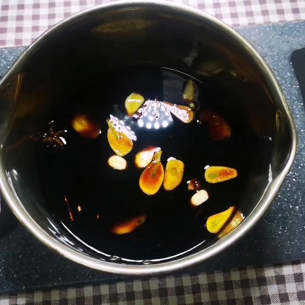 마늘, 생강, 팔각, 시나몬이 떠 있는 냄비 속에서 진한 소스가 끓어오르는 모습.
