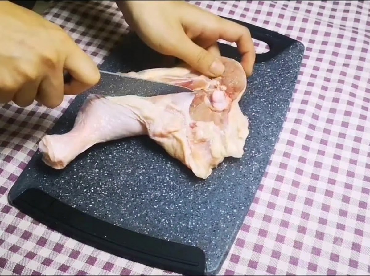 도마 위에서 생닭다리의 뼈를 제거하기 위해 날카로운 칼로 뼈를 따라 자르는 모습.