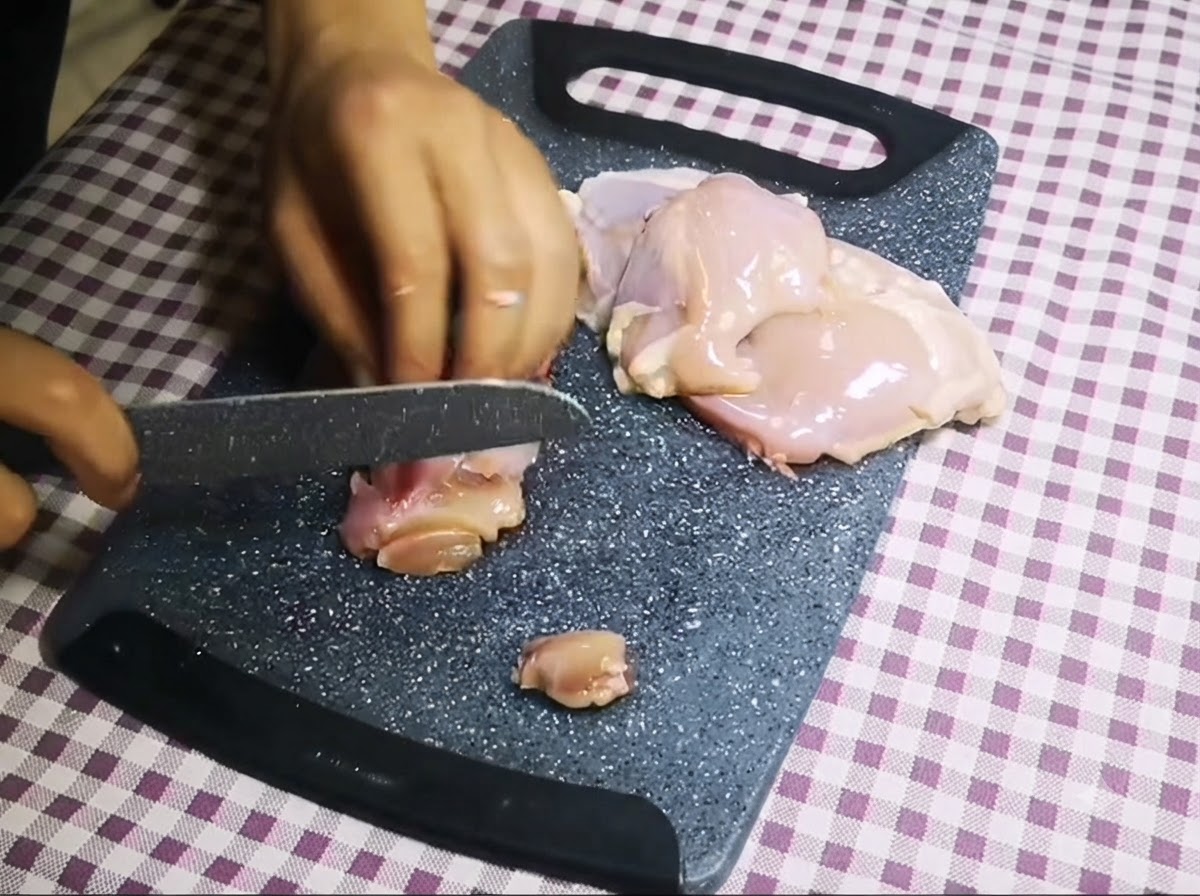 회색 도마 위에서 칼로 뼈 없는 생닭고기를 작은 조각으로 써는 모습.