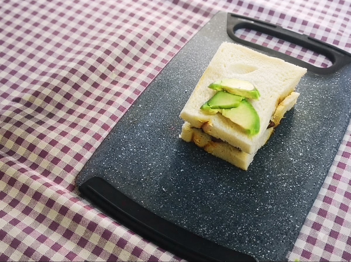 도마 위에 놓인 샌드위치 위에 썬 아보카도가 얹어져 층을 이룬 모습.