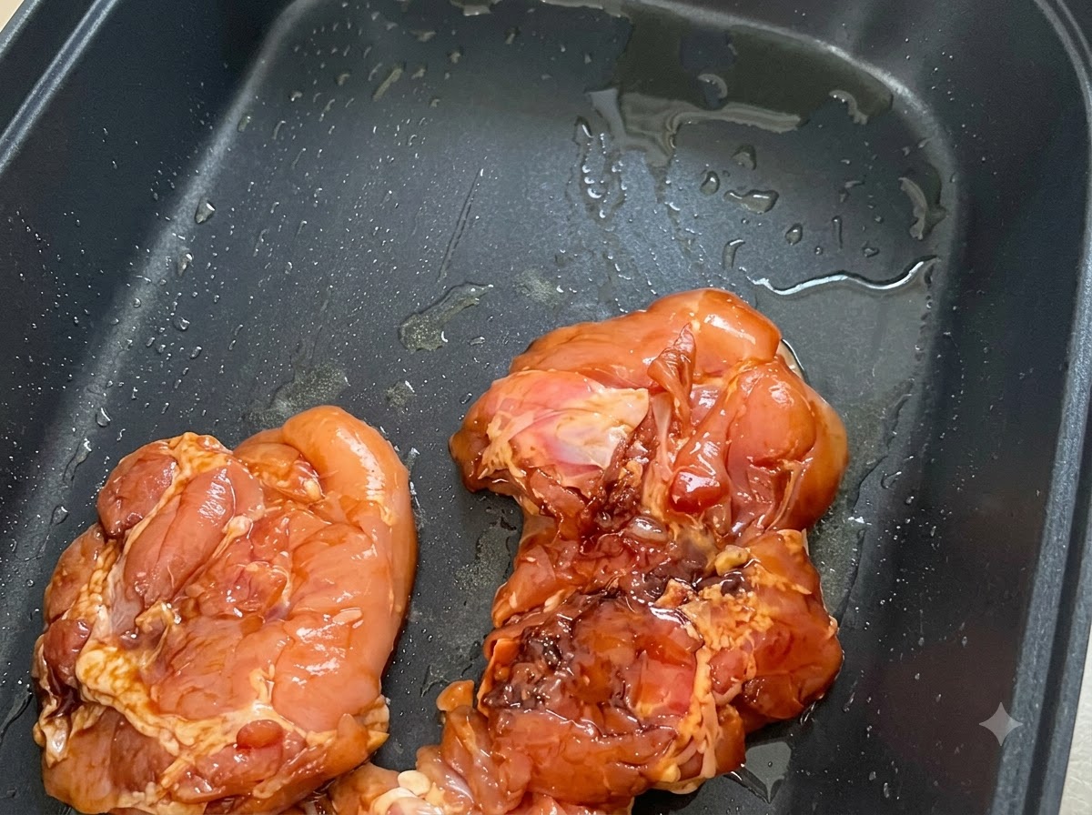 기름을 두른 검은색 논스틱 팬에 마리네이드한 닭고기 껍질이 아래로 향하게 놓인 모습