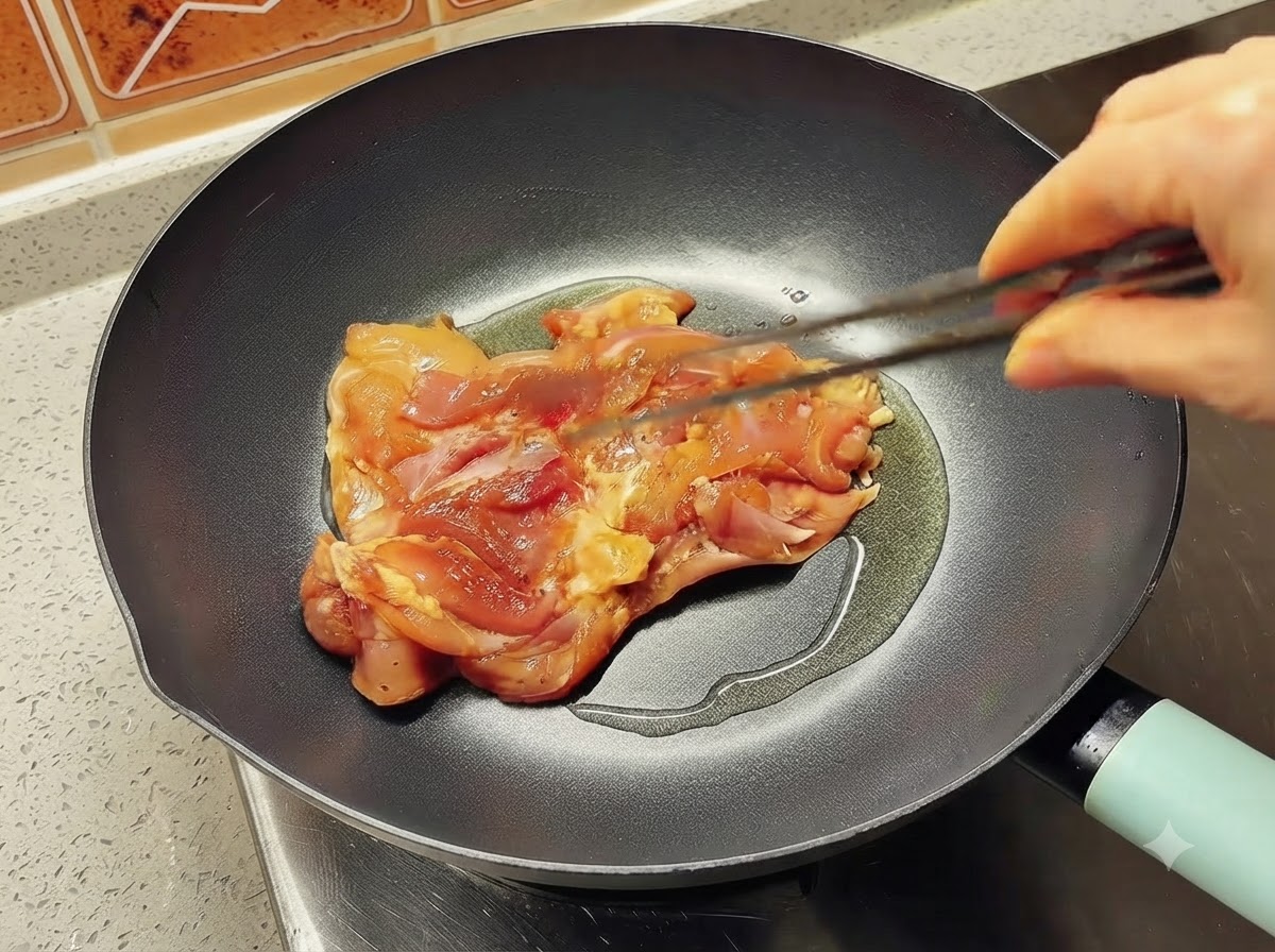집게를 이용해 식용유가 둘러진 뜨거운 팬에 양념된 닭다리살을 올리는 모습.