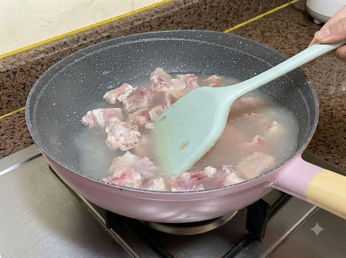 연한 파란색 실리콘 주걱으로 저어가며 냄비 안의 끓는 물에 데쳐지고 있는 돼지갈비.