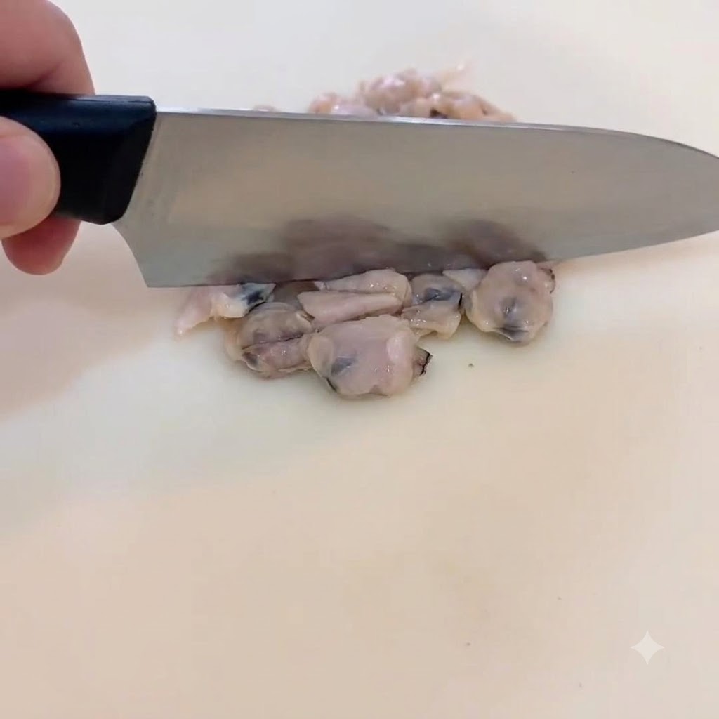 도마 위에서 익힌 조갯살을 작은 크기로 다지고 있는 셰프의 손과 칼.