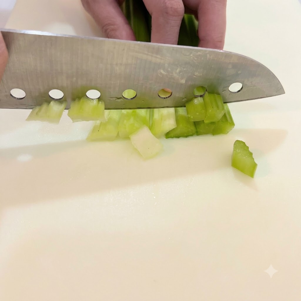 흰색 도마 위에서 밝은 초록색 셀러리를 작은 크기로 썰고 있는 모습.
