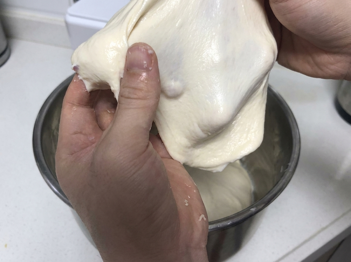 부드럽고 탄력 있는 하얀 반죽 조각을 손으로 당겨 늘리며 글루텐 강도를 보여주는 모습