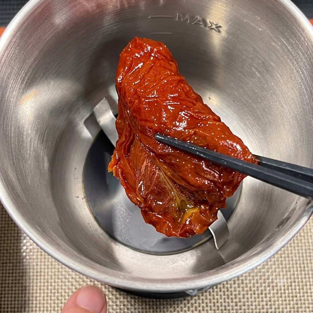 젓가락을 이용해 선드라이 토마토 조각 하나를 스테인리스 스틸 푸드 프로세서 용기에 넣는 모습.