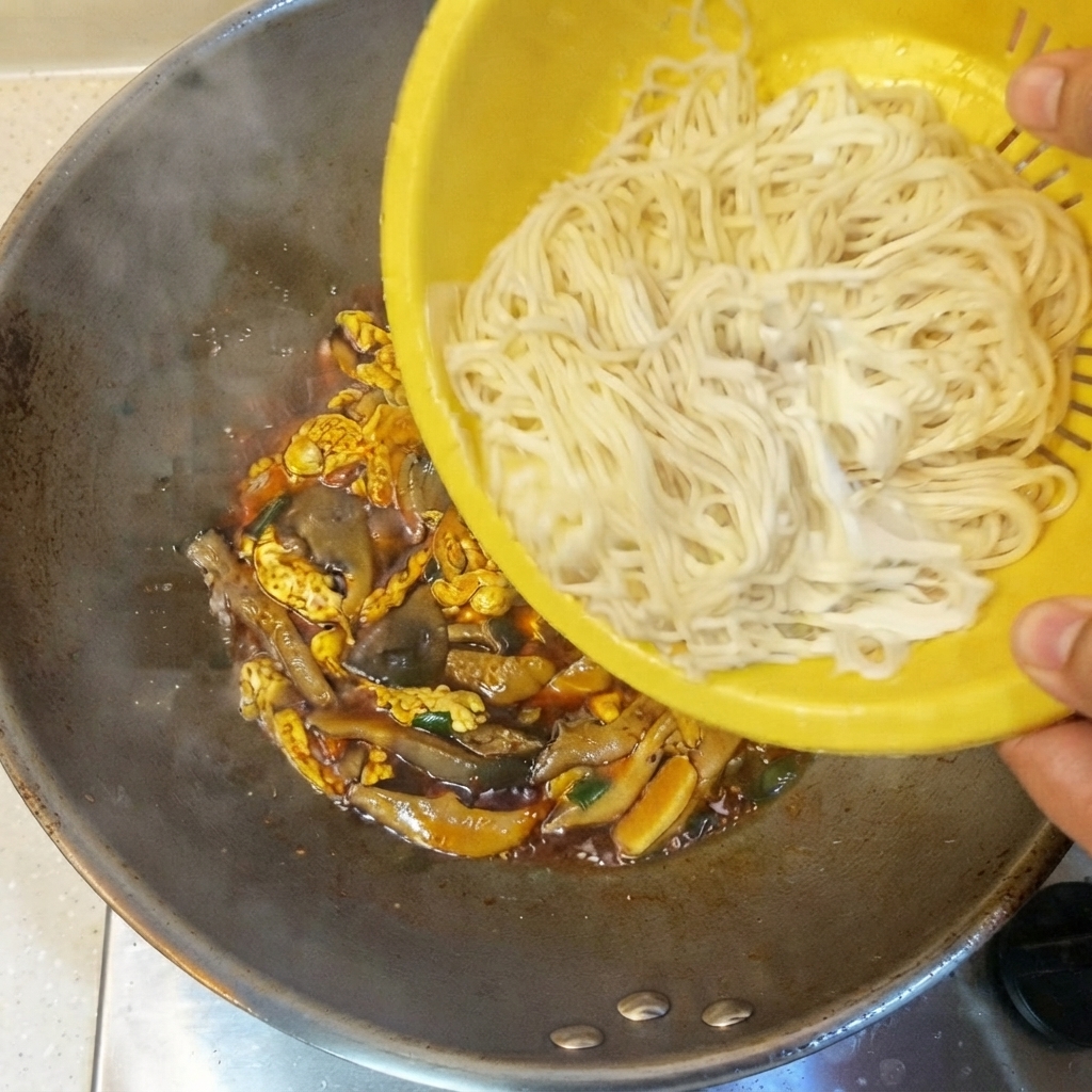 노란색 채반에서 소스와 재료가 담긴 웍으로 삶아진 얇은 면을 쏟아붓는 모습.