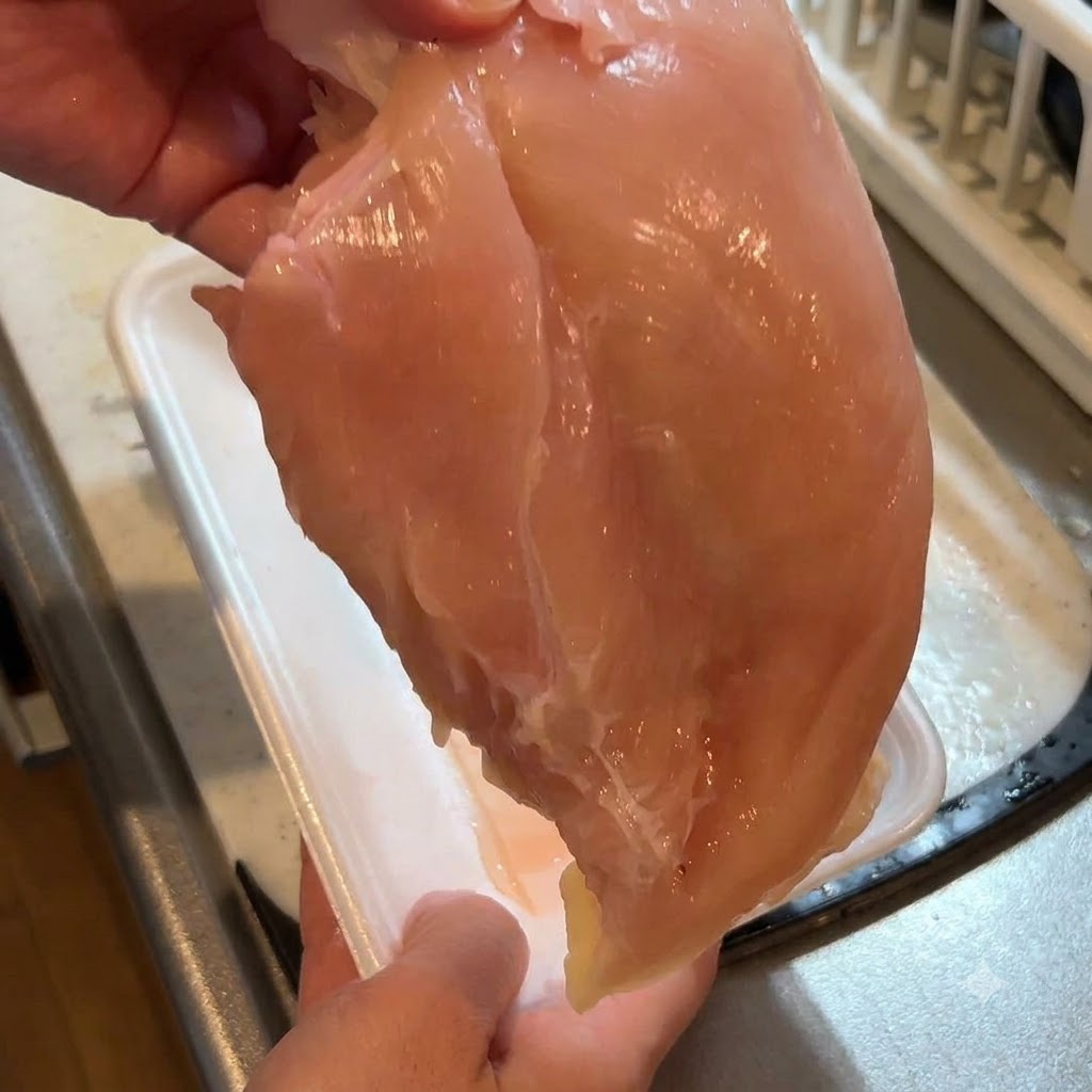 칼을 사용하여 생닭가슴살의 껍질을 벗겨내고 있는 모습.