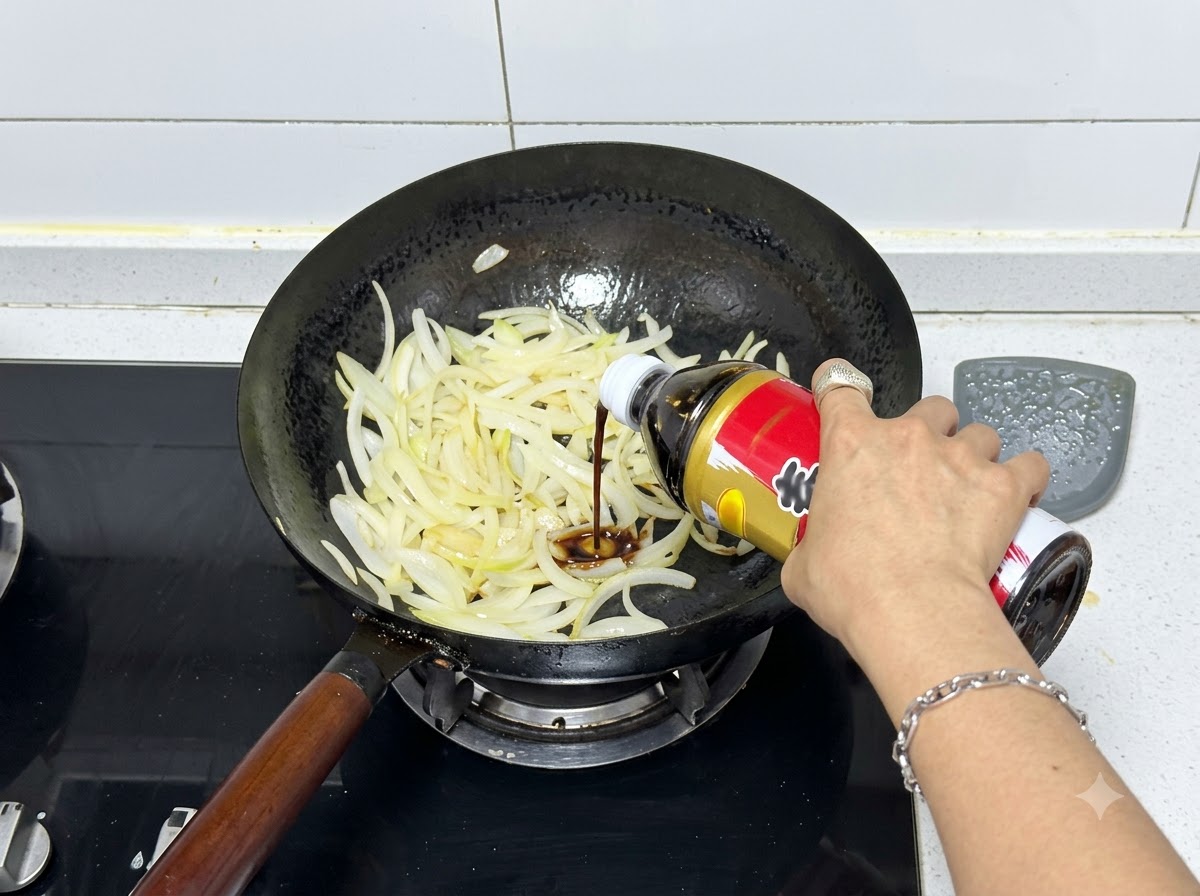 볶은 양파가 담긴 웍에 병에서 스키야키 소스가 짜여 들어가는 모습.