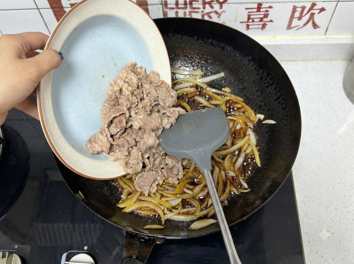미리 살짝 데친 소고기 슬라이스가 양파와 어두운 소스가 있는 웍으로 접시에서 부어지는 모습.