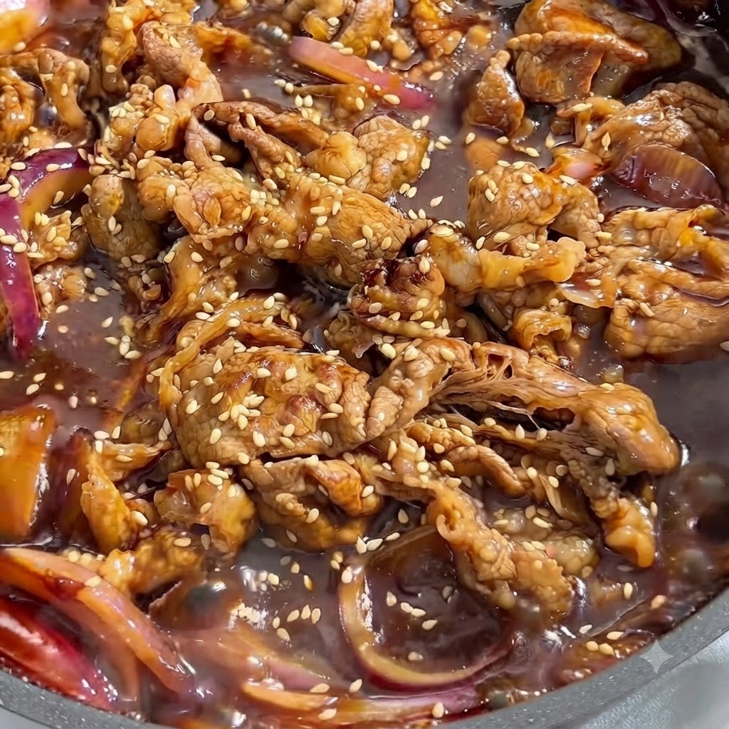 진하고 감칠맛 나는 소스에 졸여지며 하얀 참깨가 뿌려진 소고기와 적양파의 클로즈업 뷰.