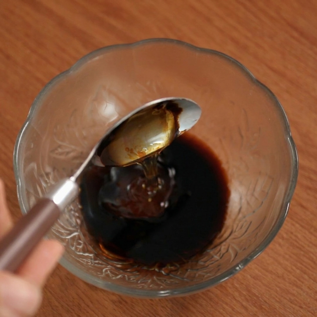 유리볼에 담긴 진한 소스에 숟가락으로 꿀을 떨어뜨리는 모습.