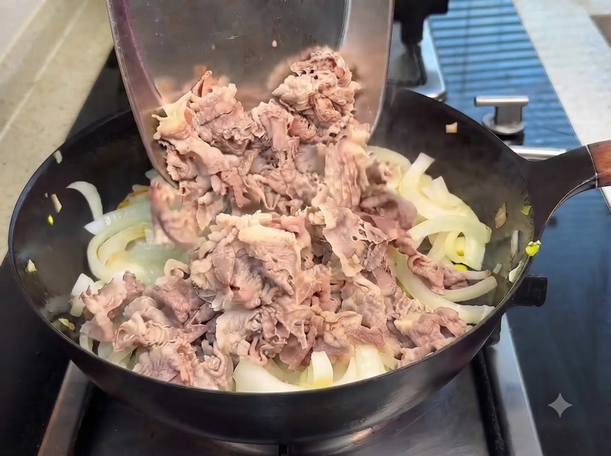 금속 뒤집개로 볶은 양파가 담긴 팬에 데친 소고기를 넣고 데리야키 소스를 붓는 모습.