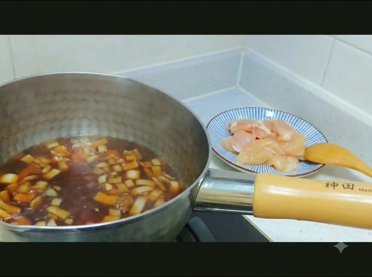 먹기 좋게 썬 날것의 닭고기와 양파를 무늬가 있는 접시에서 진한 육수가 담긴 냄비로 옮기는 모습.