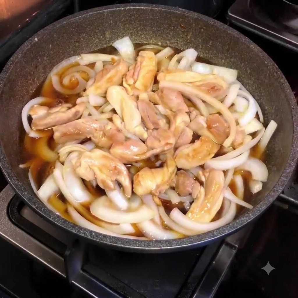 위쪽에서 내려다본, 썬 양파와 닭고기 조각, 갈색 소스로 채워진 끓는 팬의 모습.