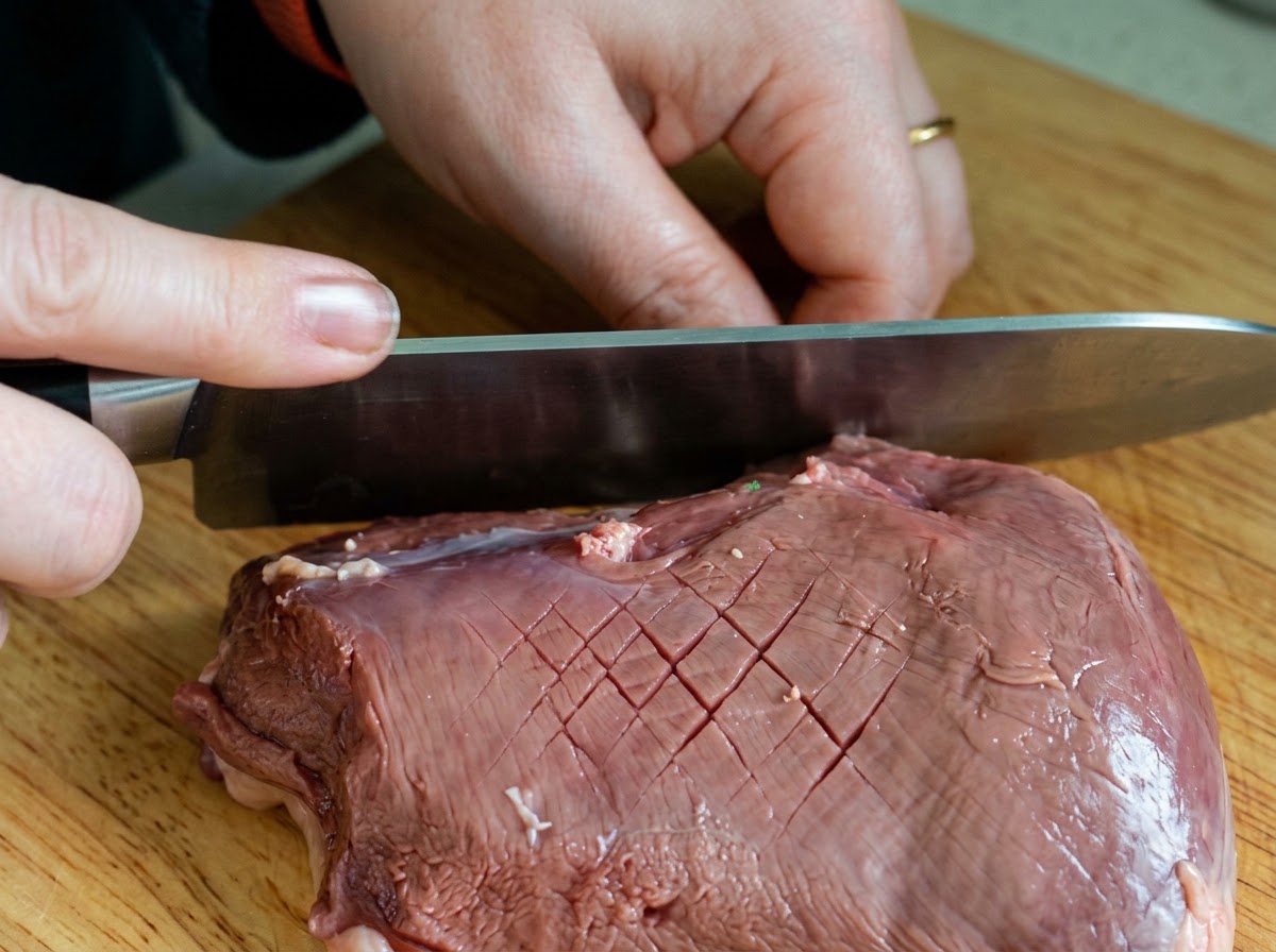 나무 도마 위에서 셰프 나이프로 생오리 껍질에 다이아몬드 격자 무늬로 칼집을 내는 모습.