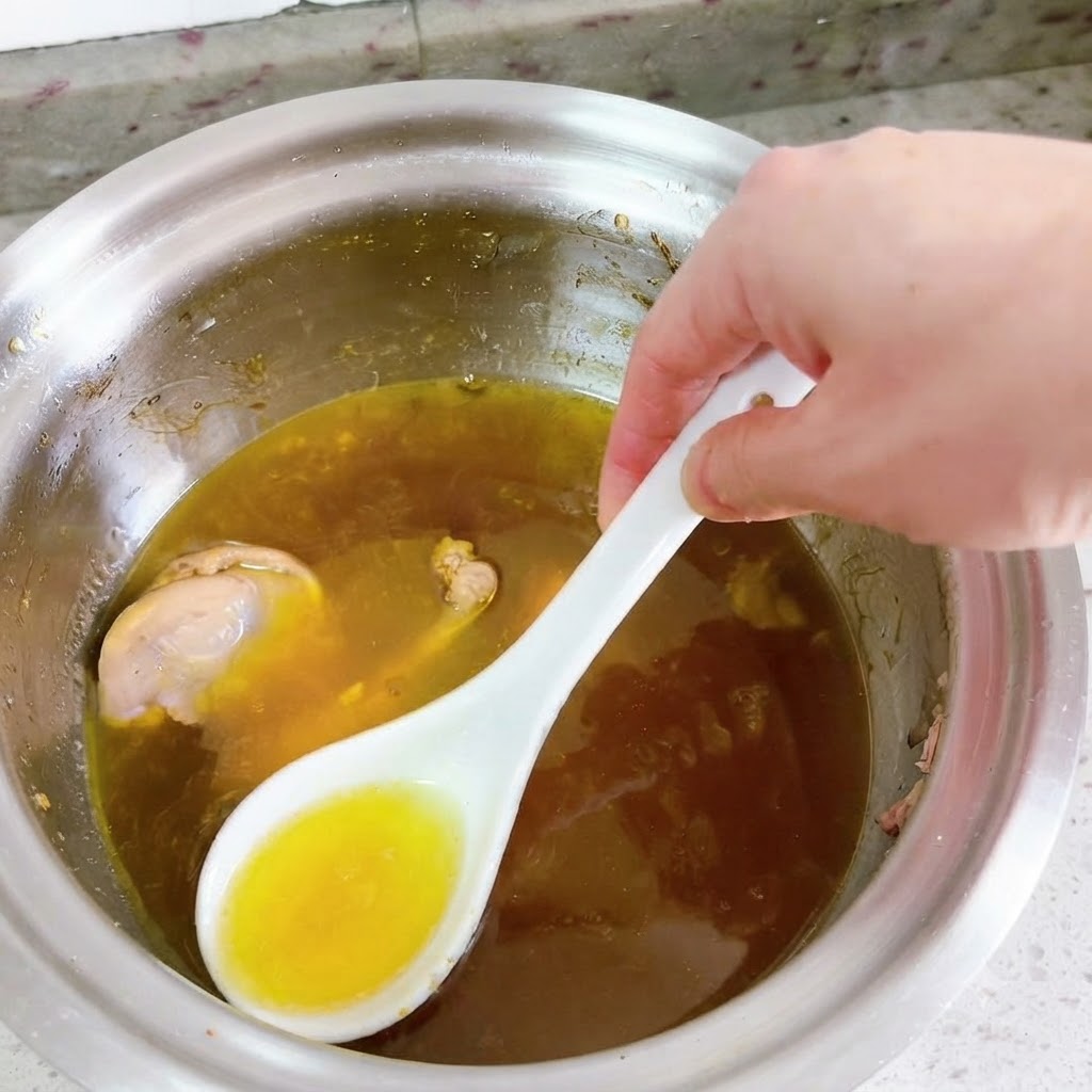 하얀 숟가락으로 끓고 있는 오리탕 표면의 밝은 노란색 기름을 걷어내고 있는 모습.