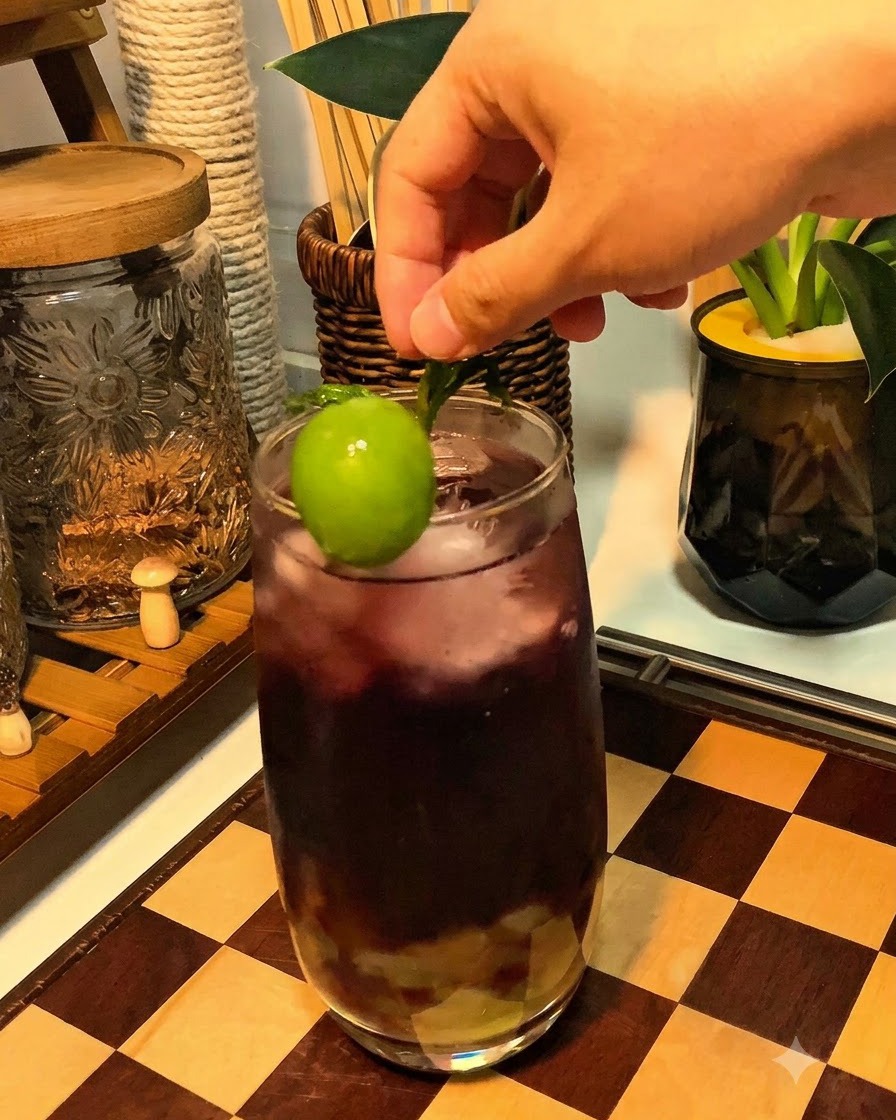 퍼플 스파클링 음료 잔 테두리에 신선한 청포도와 민트 장식을 올리는 손.
