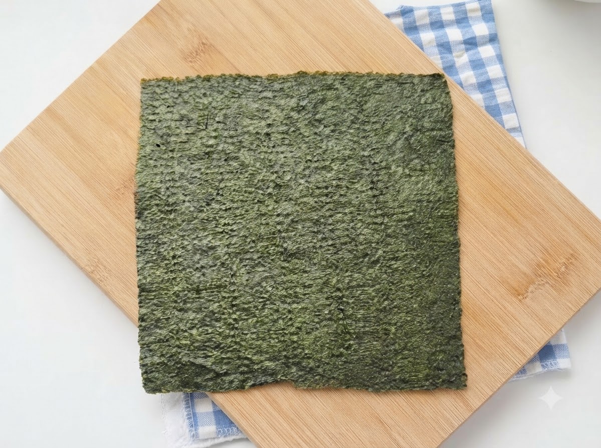 파란 체크 무늬 천이 깔린 나무 도마 위에 초록빛 김 한 장이 놓여 있는 모습.