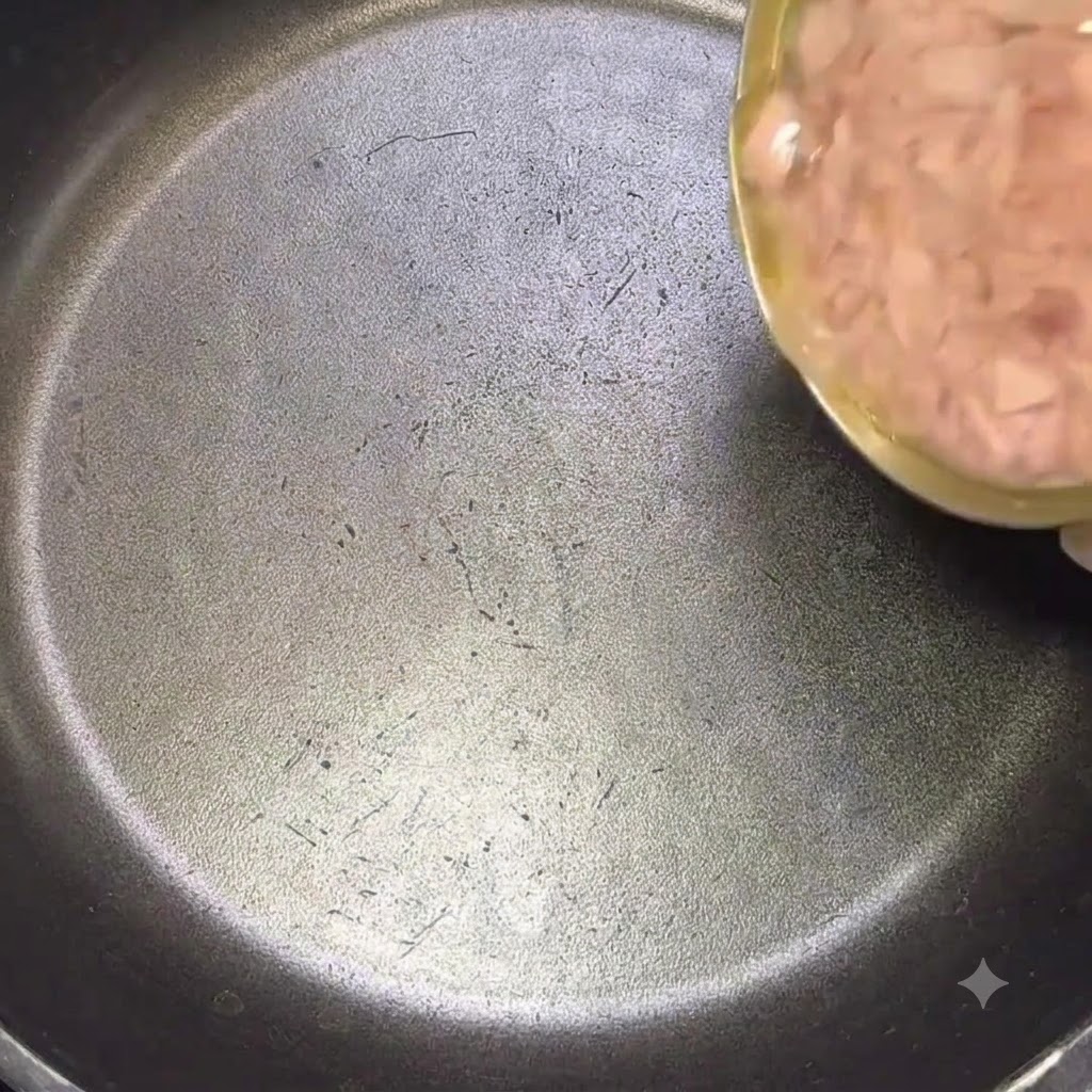 기름이 포함된 참치캔을 검은색 프라이팬에 붓는 모습.