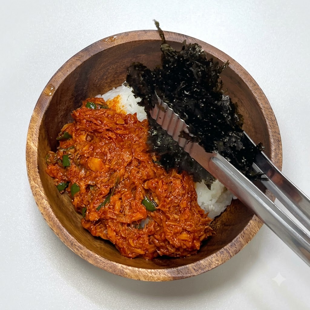 쇠 집게로 김가루를 집어 나무 그릇의 참치와 밥 옆에 놓는 모습.