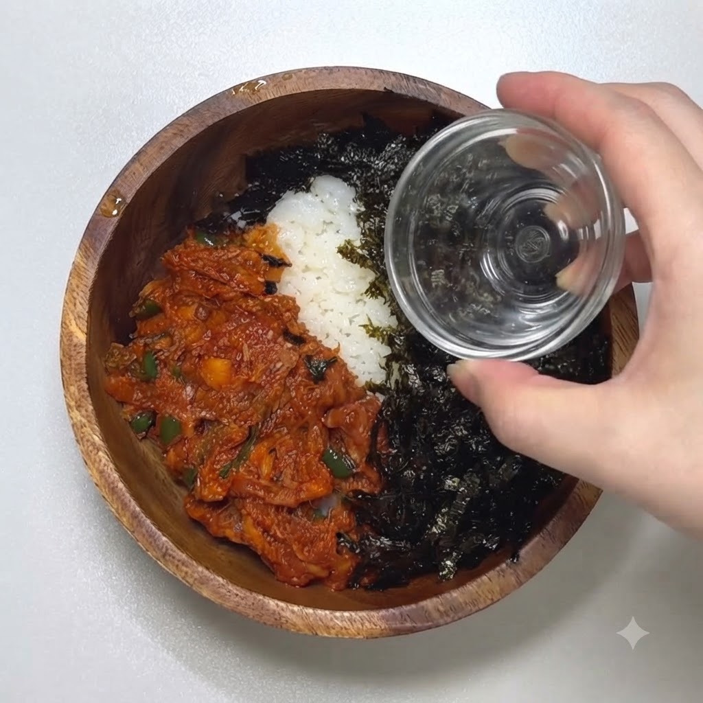 양념된 김가루와 매운 참치가 담긴 그릇 위로 작은 유리병에서 통깨를 뿌리는 클로즈업 사진.