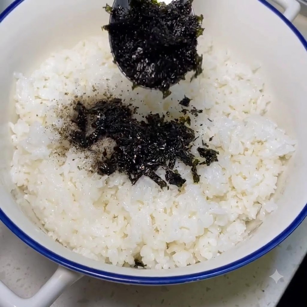 조리된 흰밥 위에 숟가락으로 김가루를 솔솔 뿌리는 모습