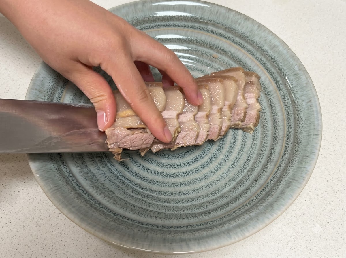 칼을 이용해 질감이 느껴지는 회색 접시 위로 썬 삼겹살 조각들을 옮겨 담고 있습니다.