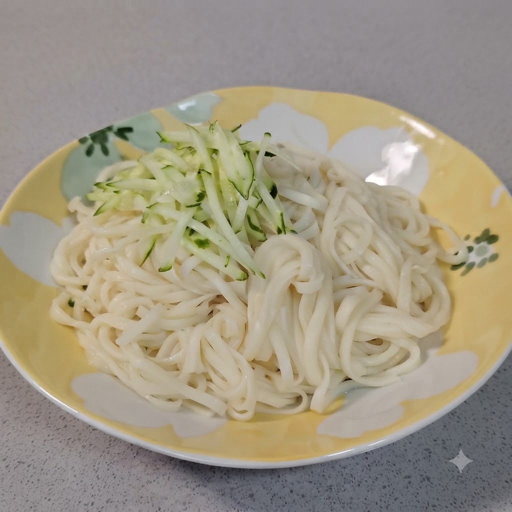 장식된 접시에 담긴 하얀 삶은 면 위에 신선한 초록색 오이채 한 움큼을 얹고 있는 모습.