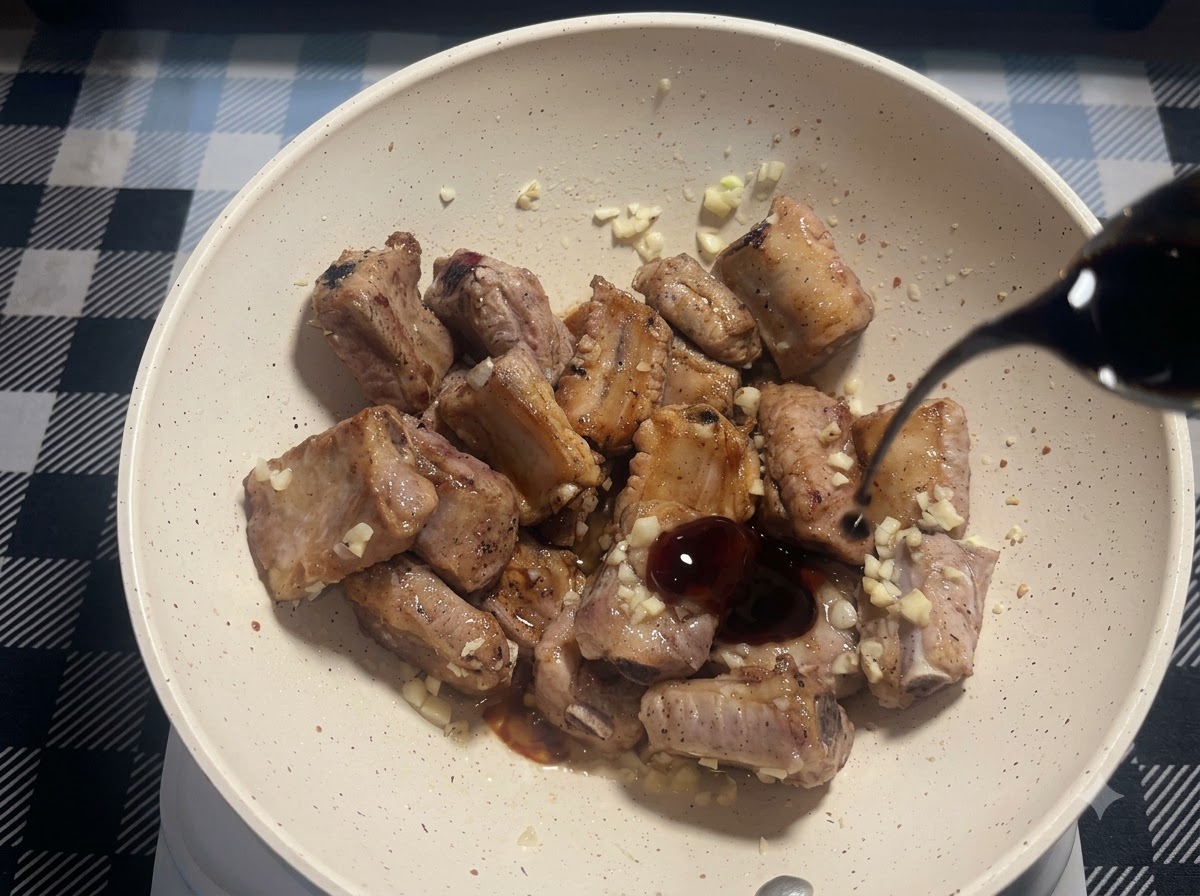 구운 돼지 갈비와 다진 마늘이 있는 팬 안으로 노두유가 가늘게 부어지고 있는 모습.