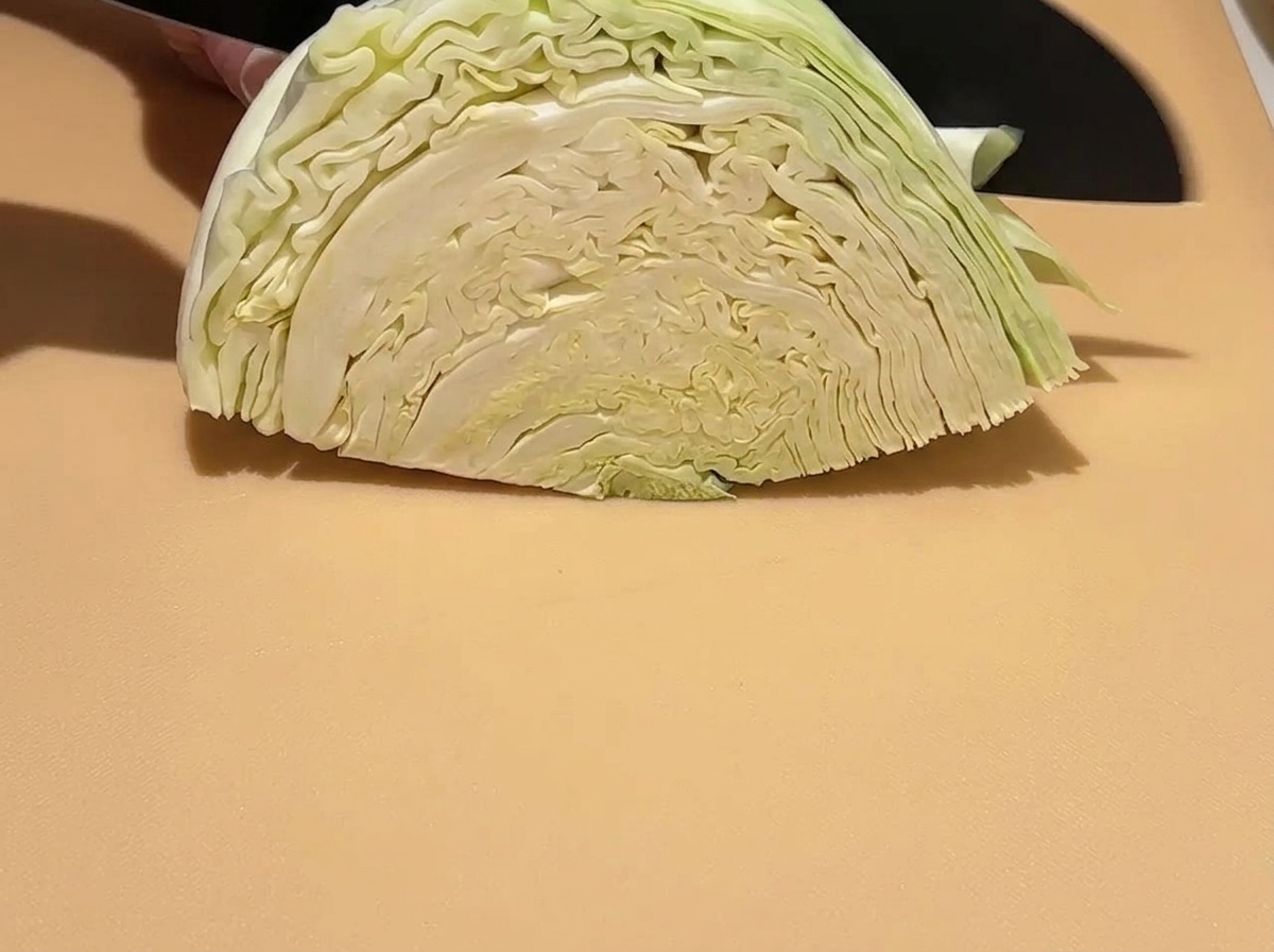 도마 위에서 생양배추를 칼로 큼지막하게 써는 모습.