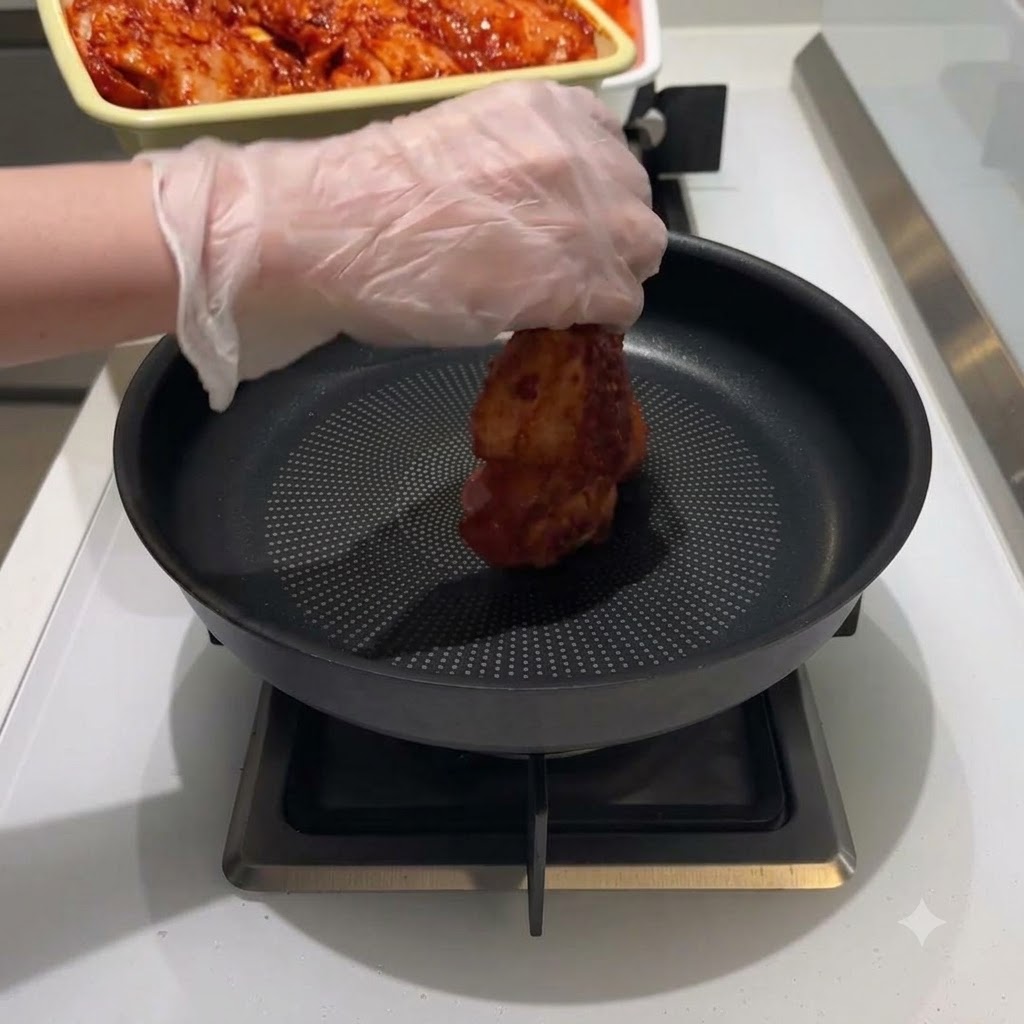양념에 재운 닭고기를 검은색 프라이팬 중앙에 올리는 모습.