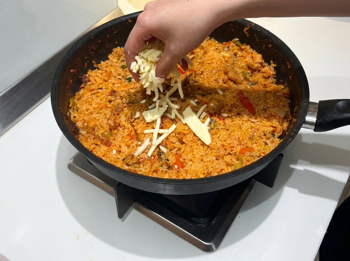 매콤하게 볶아진 붉은 볶음밥 위에 모짜렐라 치즈를 한 줌 듬뿍 뿌리는 모습.