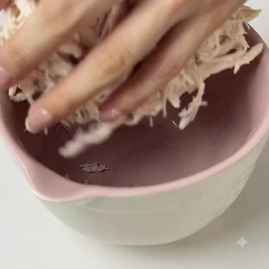 분홍색 믹싱 볼 안에서 찢은 닭가슴살에 초록색 페스토 소스를 넣고 손으로 버무리는 모습.